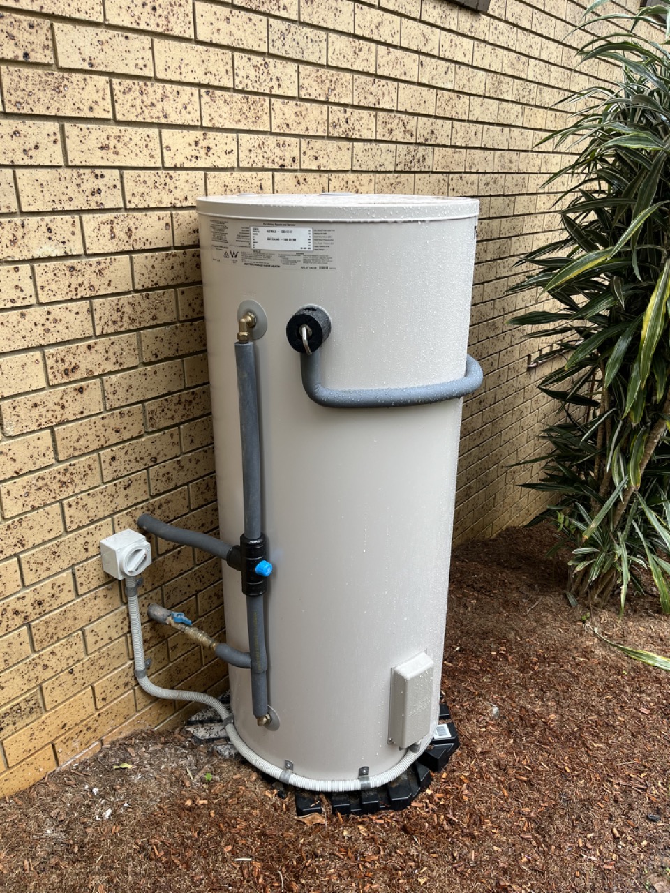 New electric hot water cylinder installed against a brick wall
