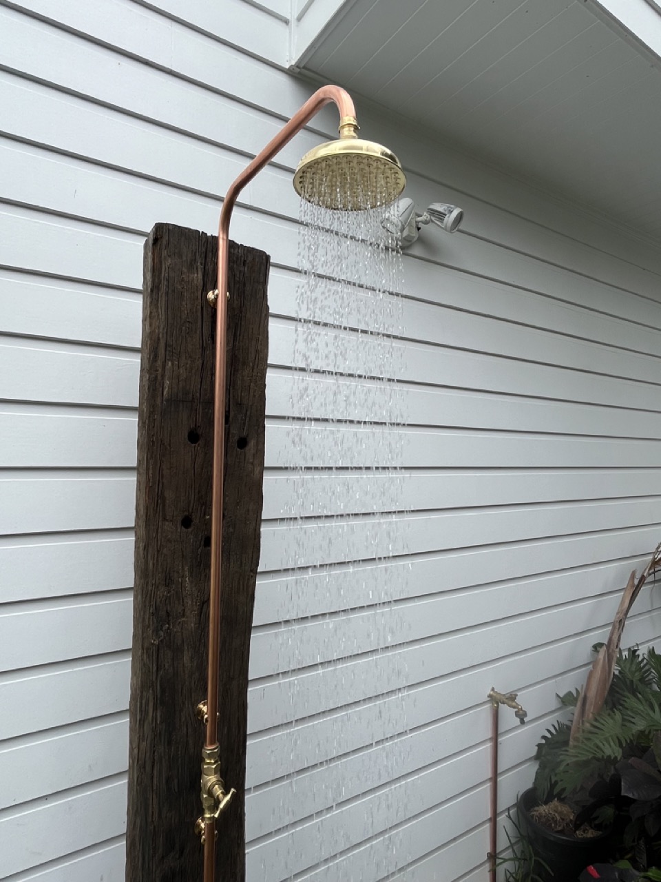 Brass outdoor shower on a timber post with water running