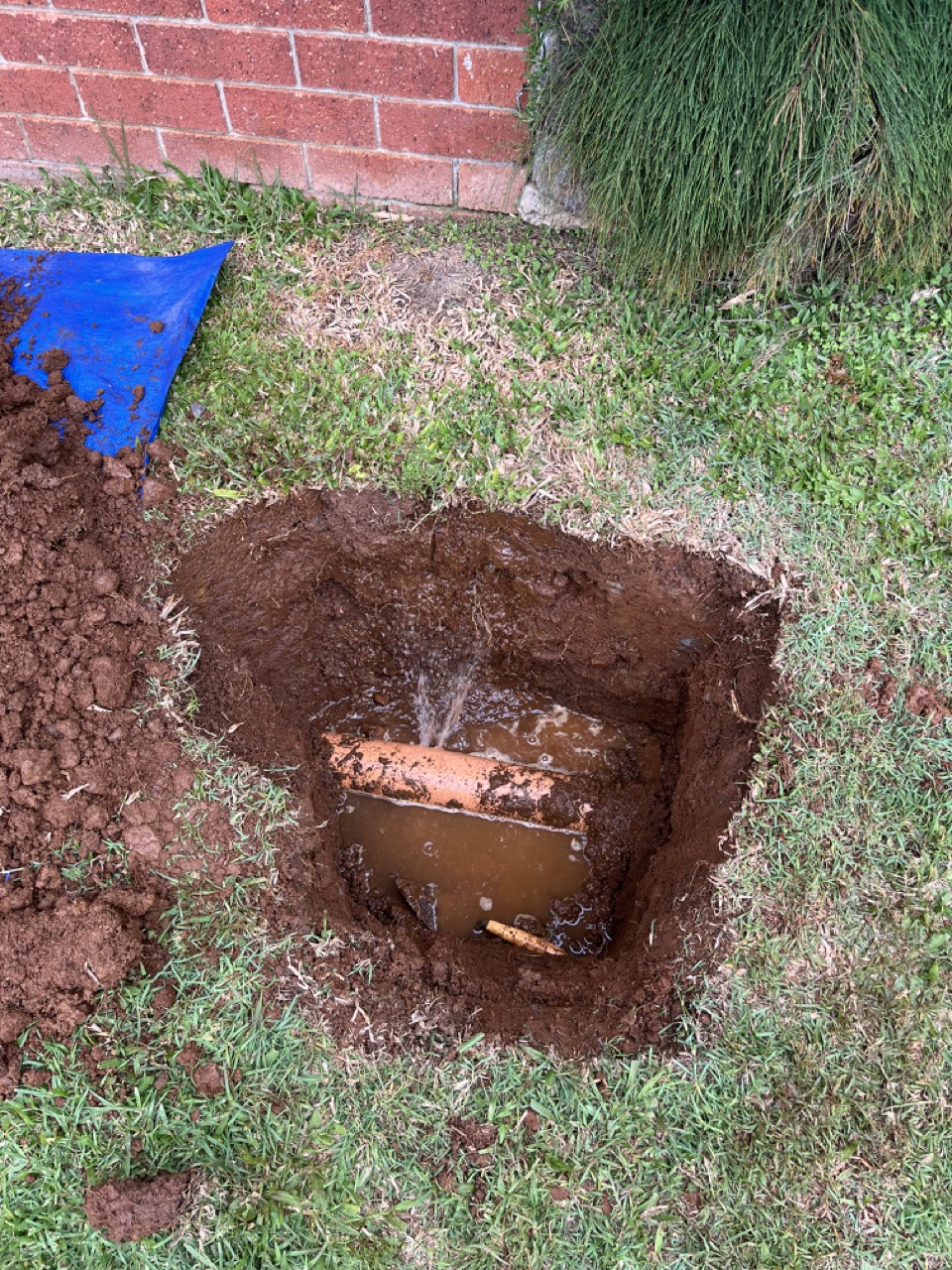 Hole dug in a lawn exposing an underground pipe being repaired